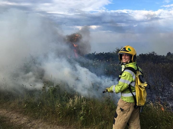 image of a grass fire with a female firefighter with a hose and backpack filled with water