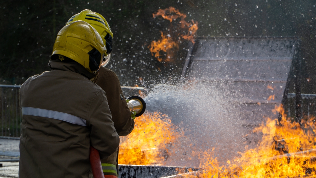 Image of a firefighter with a hose extinguishing flames from a fire