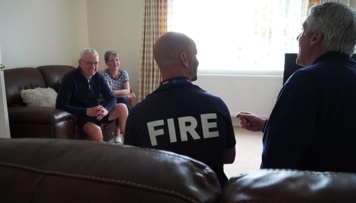 A picture of two people sitting on a couch smiling whilst talking to two firefighters also sat on an adjacent couch