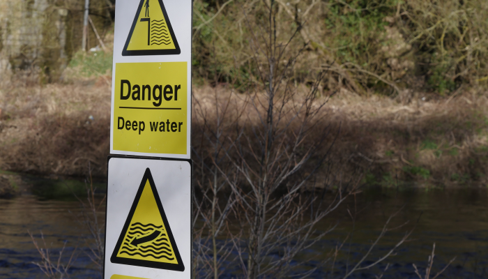 A picture of a danger deep water sign  next to a river