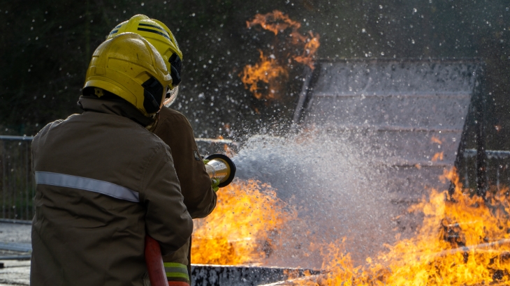 Image of a firefighter with a hose extinguishing flames from a fire