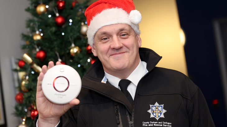 Group Manager Jon Singleton wearing a santa hat and holding a smoke alarm with a Christmas tree in the background. 