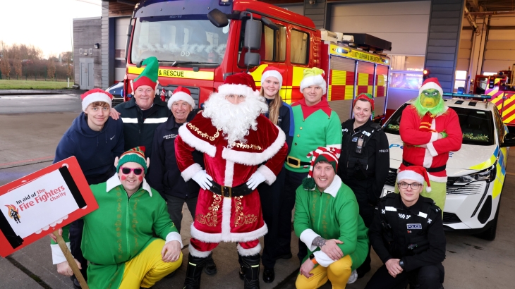 Santa surrounded by elves, fire cadets, police officers and the grinch. Fire engine and police car parked in the background.