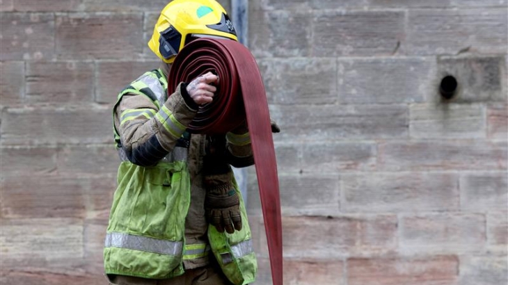 Firefighter wearing fire kit and holding a hose reel. 