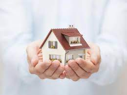 a pair of hands cradling a small house against a white shirt