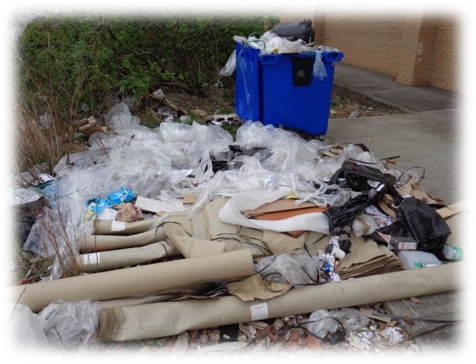 Waste materials on the ground, next to an overflowing large outdoor bin