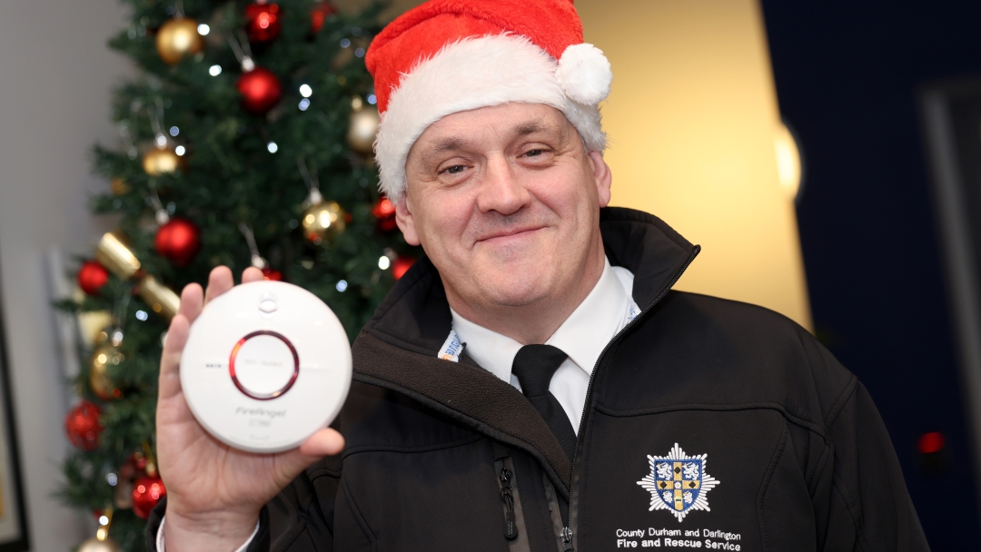 Group Manager Jon Singleton wearing a santa hat and holding a smoke alarm with a Christmas tree in the background. 